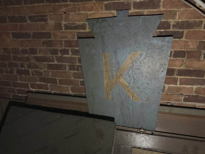 A keystone shaped blue sign with a large K on it.