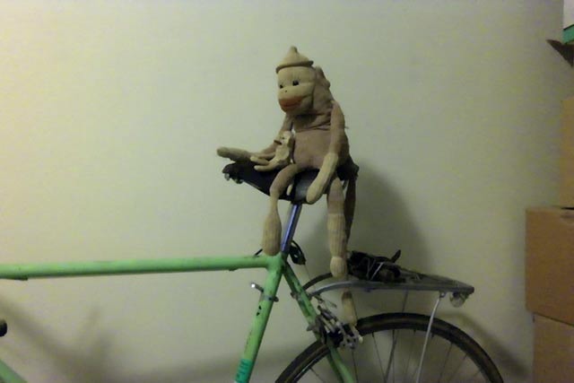 Two sock monkeys sitting on a bicycle.