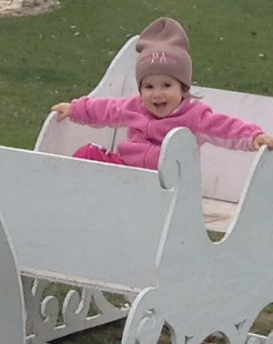 Grand daughter smiling in a wooden sleigh at the park.